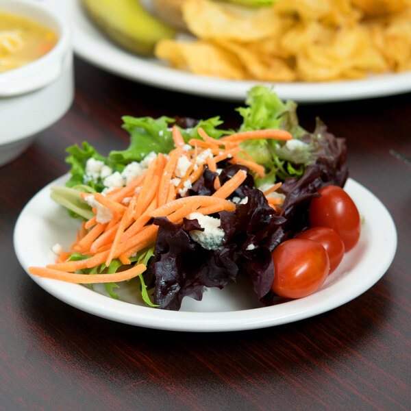 A Libbey white porcelain plate with a salad and soup on a table.