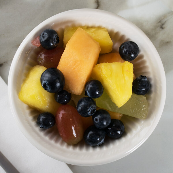 A Tuxton Hampshire eggshell embossed china fruit bowl filled with blueberries, grapes, and pineapple on a marble table.