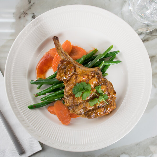 A Tuxton Hampshire china plate with meat and vegetables and sauce on it.