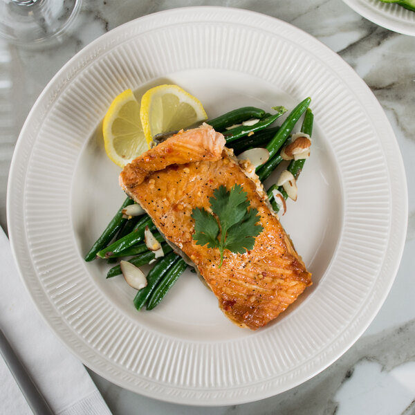 A Tuxton Hampshire china plate with a piece of meat and green beans on it.