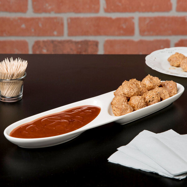 A Libbey white porcelain 2 well serving tray with food and sauce on a table.