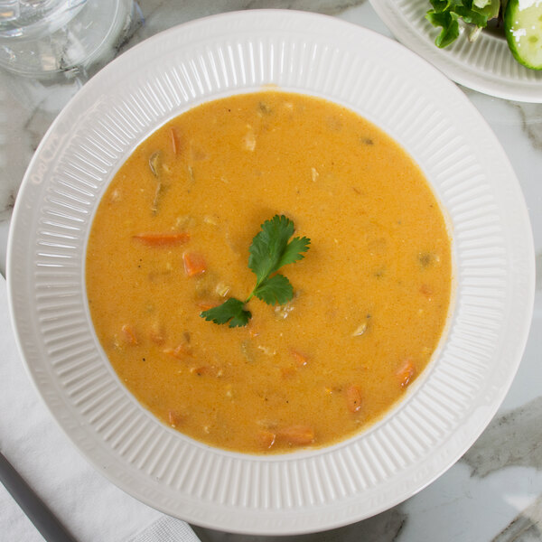 A Tuxton Hampshire eggshell embossed china soup bowl filled with soup and garnished with herbs on a white plate.