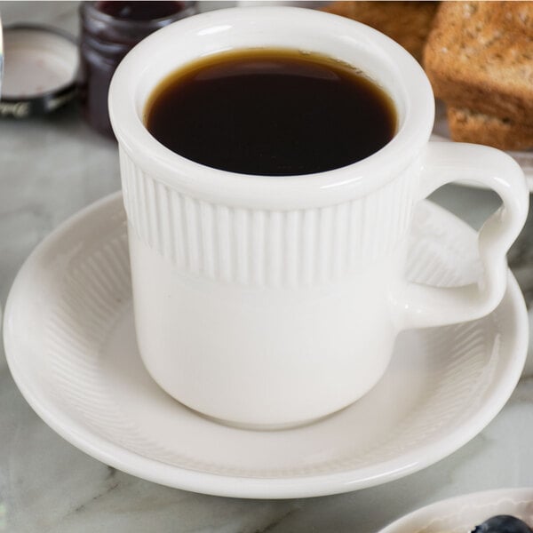 A cup of coffee sits on a white Tuxton Hampshire saucer.