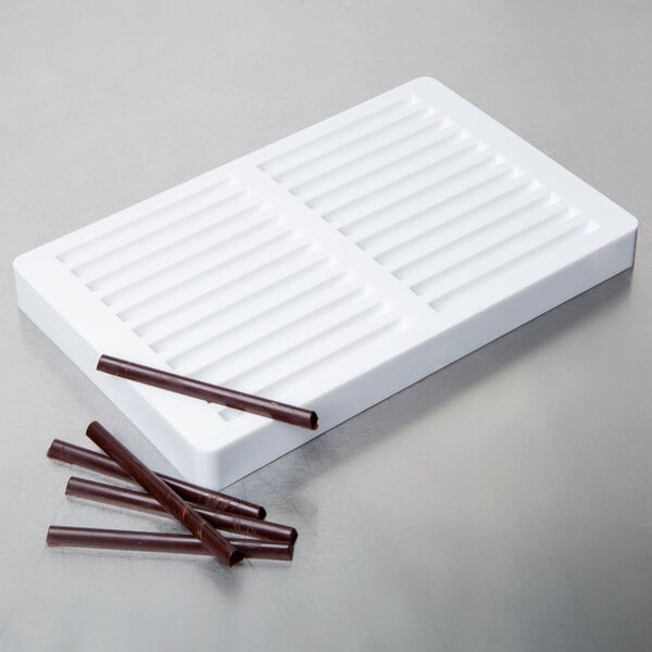 A white rectangular Martellato chocolate mold with brown sticks on it.