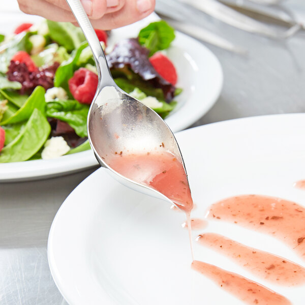 A Mercer Culinary plating spoon over a plate of salad.