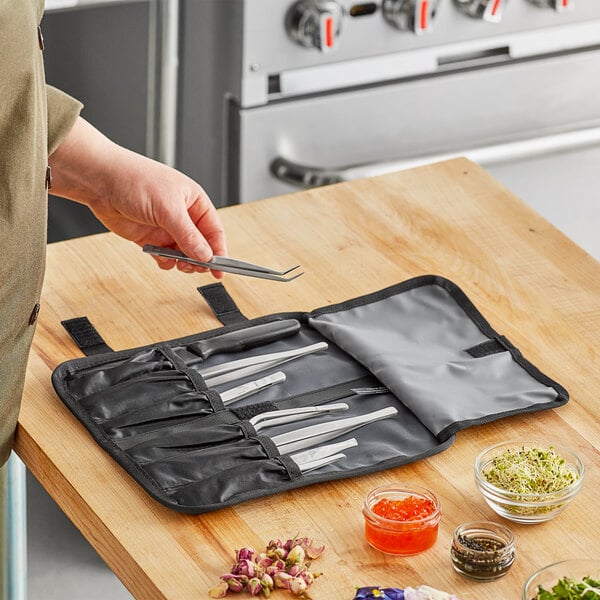 A person using Mercer Culinary precision plating tongs to place black seeds in a glass container.