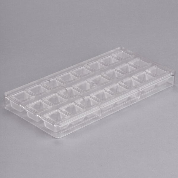A clear plastic Chocolate World mold with small square compartments.