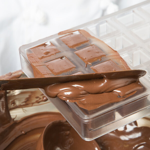 A Chocolate World polycarbonate chocolate mold with a wooden square shape being poured into.