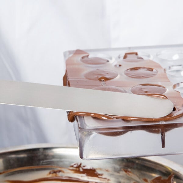 A person holding a white Matfer Bourgeat chocolate mold over a tray of chocolate.