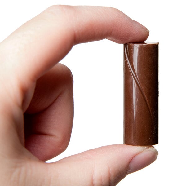 A hand holding a Chocolat Form polycarbonate chocolate mold filled with chocolate.
