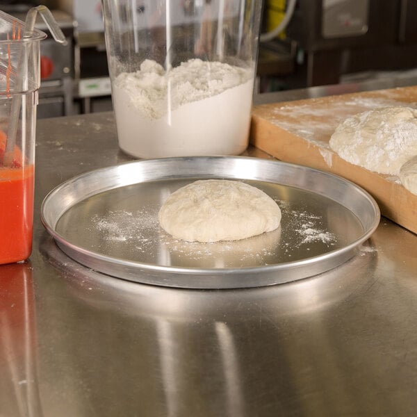 An American Metalcraft heavy weight aluminum pizza pan with dough on it on a table.