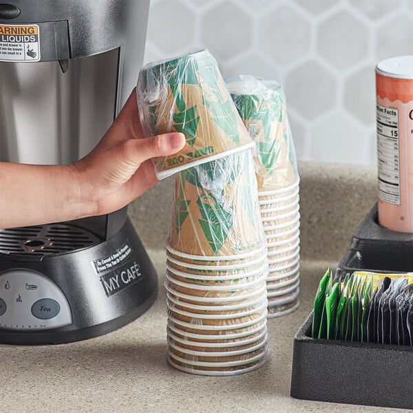 A hand holding a stack of Lavex Kraft paper hot cups.