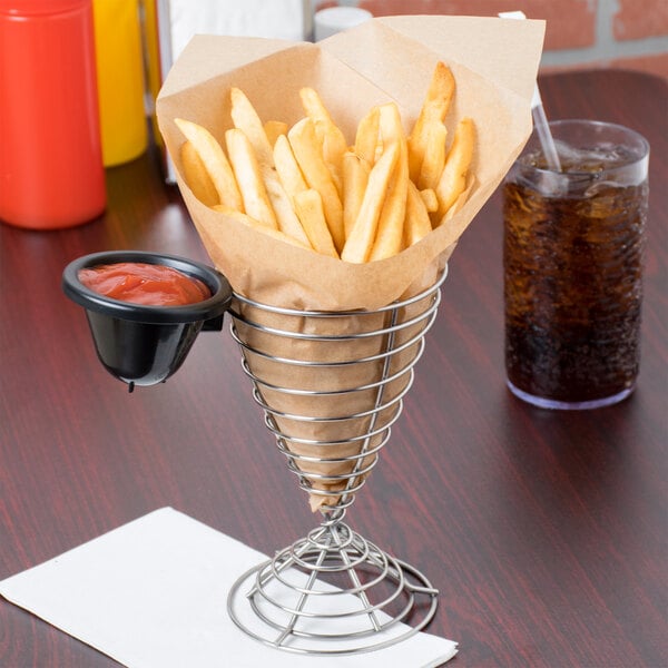 A Clipper Mill stainless steel wire cone basket filled with french fries with ketchup and a drink on a table.