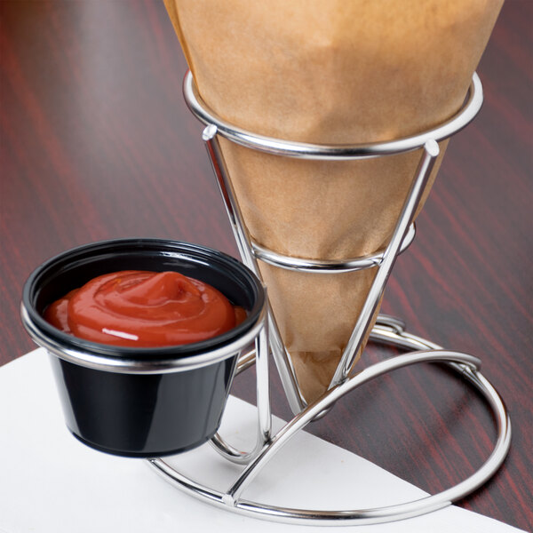 A Clipper Mill stainless steel wire cone basket with ramekin holder holding a cup of sauce on a table.