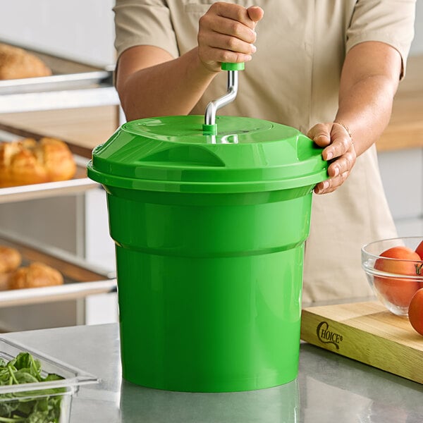 A large green 2.5-gallon salad spinner with a hand crank being used on a kitchen counter.