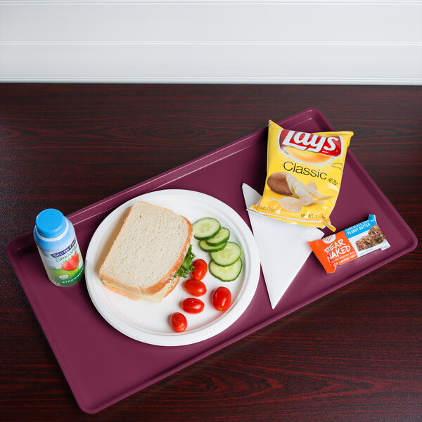 A Cambro burgundy dietary tray with a sandwich, chips, and a bottle on it.