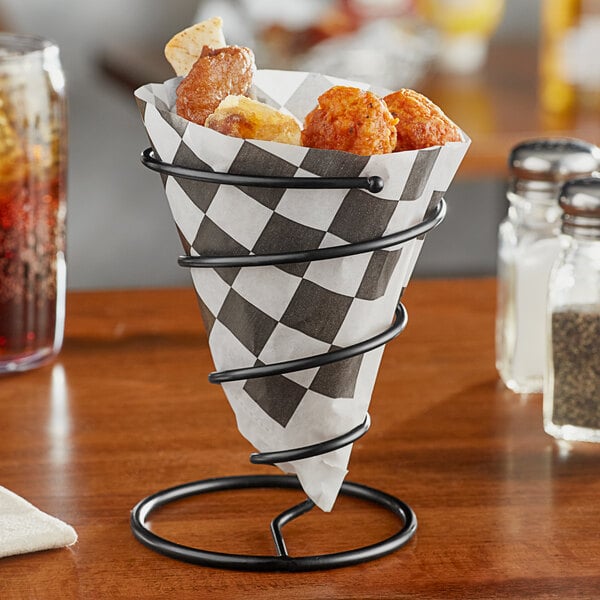 A black wrought iron cone basket with food on a table.