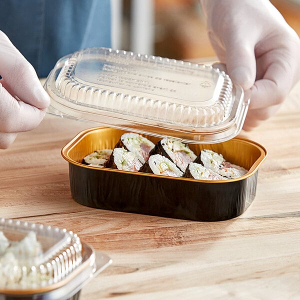 A hand holding a plastic container of sushi with a clear plastic dome lid.