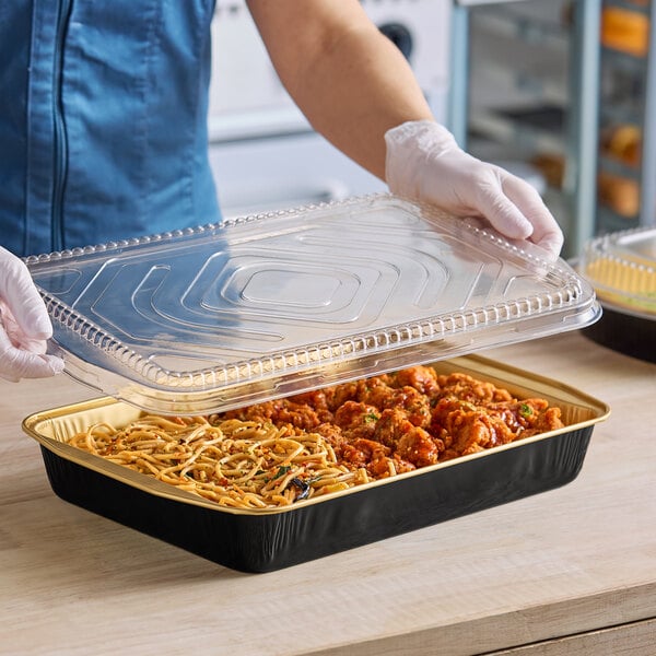 A person in gloves holding a Durable Packaging black and gold aluminum tray with food.