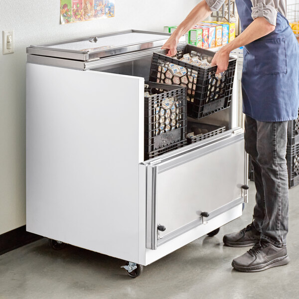 A man putting a bin of milk in an Avantco School Milk Cooler.