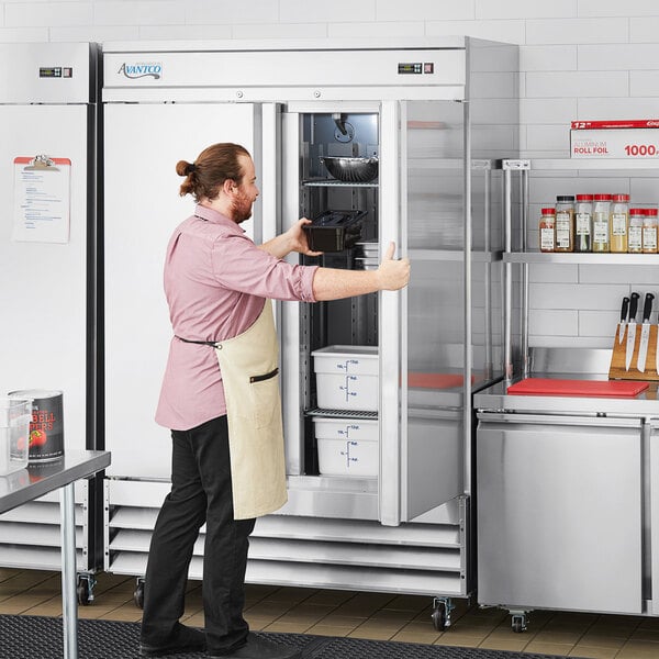 A man standing in front of an Avantco stainless steel reach-in freezer in a professional kitchen.