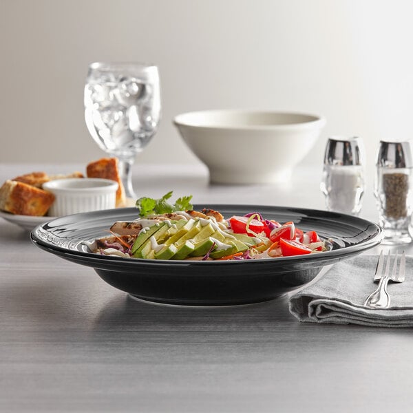 A close up of a Tuxton Concentrix black china bowl with food and a fork on a table.