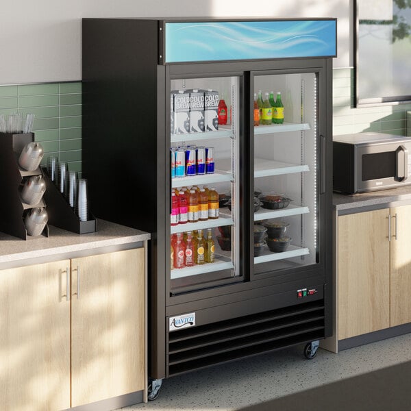 A black sliding glass door merchandiser refrigerator with LED lighting, stocked with beverages and food items.