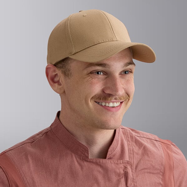 A man wearing a khaki 6-panel baseball cap and a pinkish chef coat.