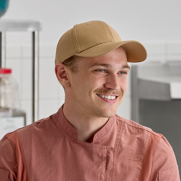A khaki 6-panel cap worn by a person in a kitchen setting.
