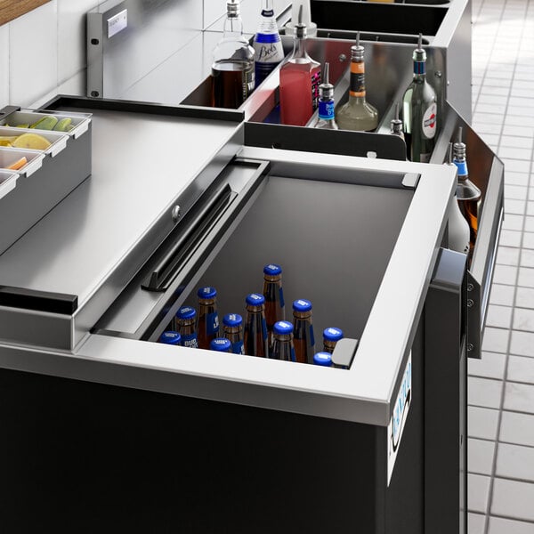 An Avantco black horizontal bottle cooler on a counter in a cocktail bar with bottles inside.