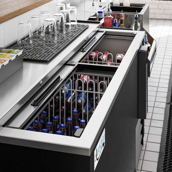 An Avantco black horizontal bottle cooler on a counter with bottles and glasses inside.