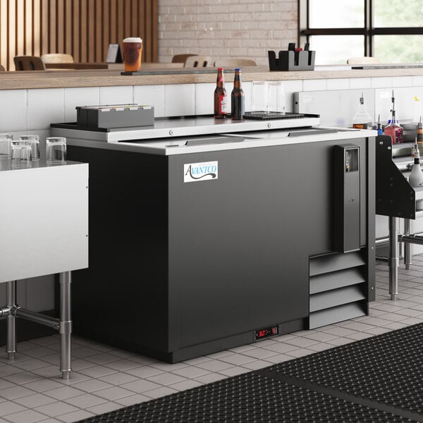 A black Avantco horizontal bottle cooler on a counter with a stainless steel top and door.
