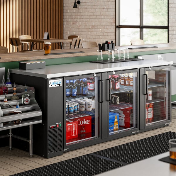 An Avantco black counter height back bar refrigerator with glass doors filled with drinks and bottles.