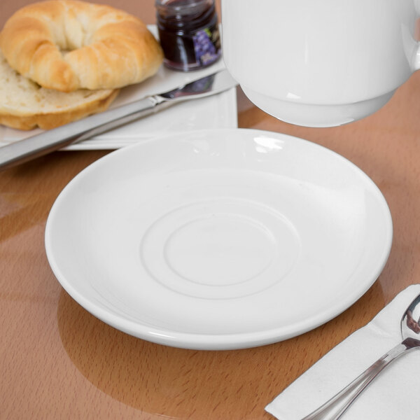A white saucer with a white Libbey soup cup on it on a table.