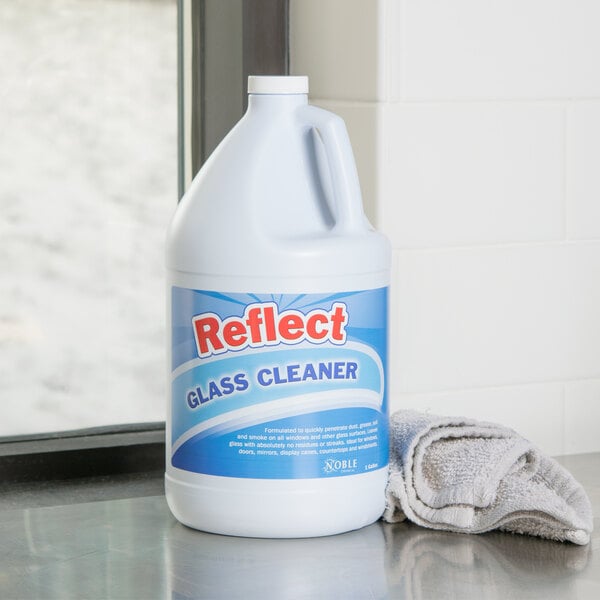 A white bottle of Noble Chemical Reflect Glass Cleaner with a blue label on a counter next to a towel.