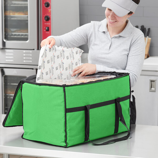 A woman holding a green Choice insulated food delivery bag with black trim containing food.