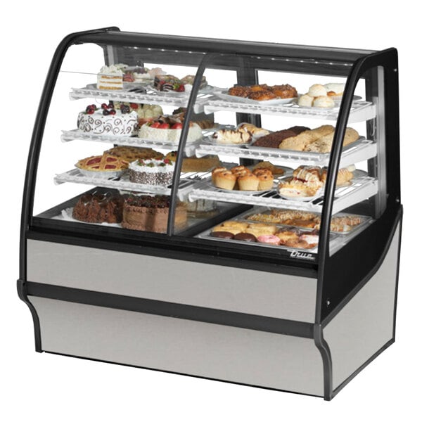 A True stainless steel curved glass dual zone refrigerated bakery display case on a counter with cakes inside.