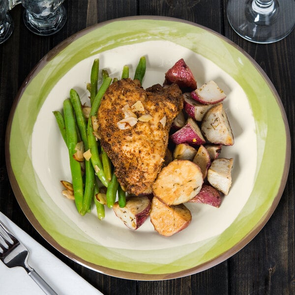 A Kanello Diamond Ivory melamine plate with green edge holding chicken, potatoes, and green beans with a fork and knife.