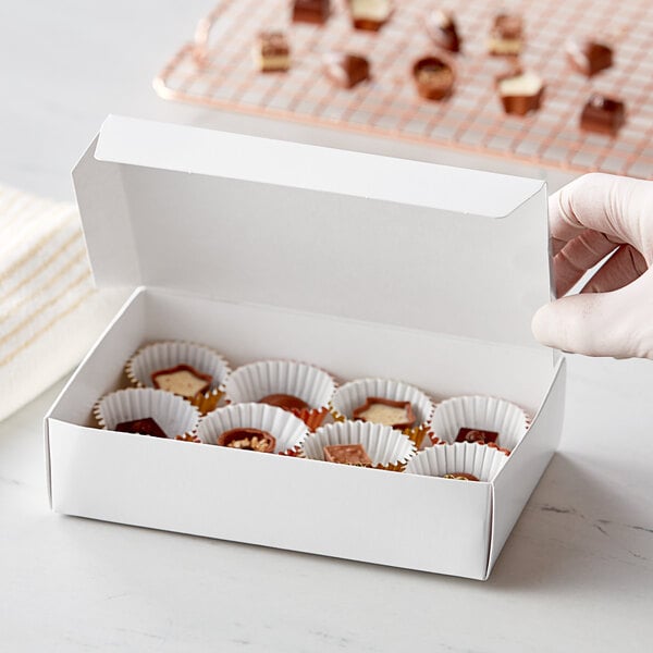 A hand holding a 7 1/4" x 4 5/8" white 1-piece candy box filled with chocolates.