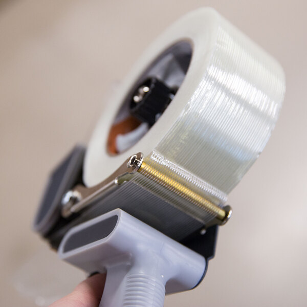 A person's hand holding a roll of Shurtape general purpose fiberglass reinforced strapping tape.