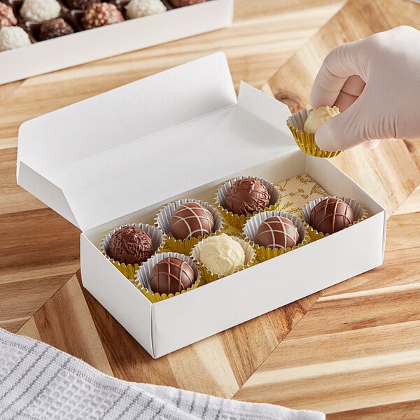 A hand holding a white 1-piece candy box filled with chocolates.