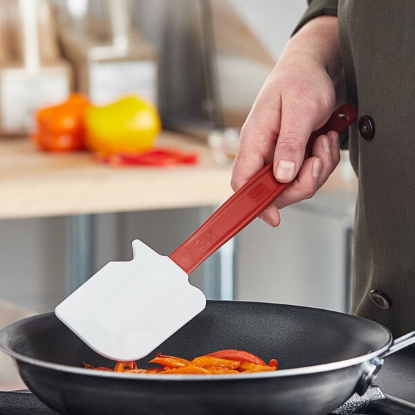 A hand using a Rubbermaid red high temperature silicone spatula to stir food in a pan.
