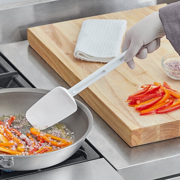 A person using a white Rubbermaid spoonula to stir vegetables in a pan.