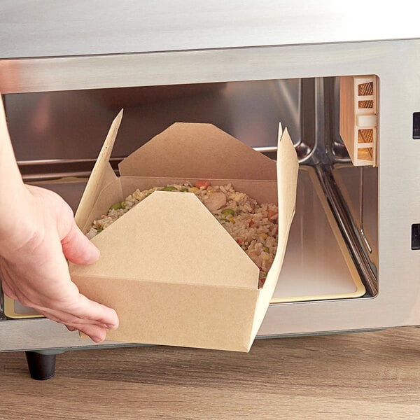 A hand holding a Choice Kraft microwavable folded paper take-out container of food.
