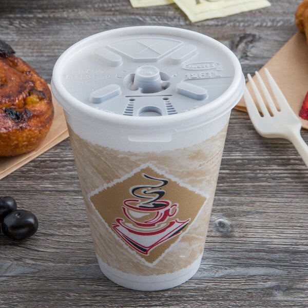 A Dart foam coffee cup with a translucent lid and straw slot next to a pastry.