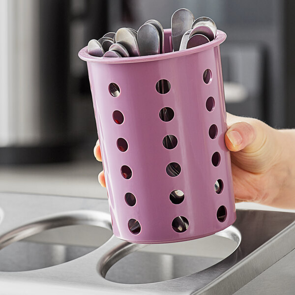 A hand holding a violet Steril-Sil flatware cylinder filled with spoons.