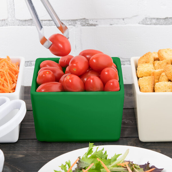 A bowl of salad with tomatoes and croutons in a green Tablecraft square container.