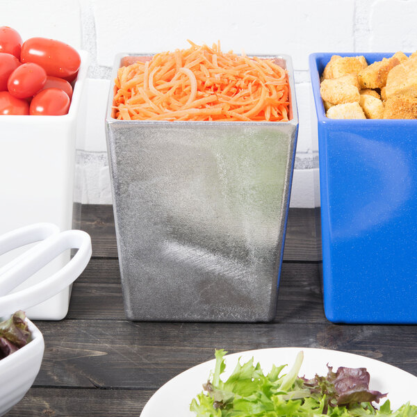 A white table with a Tablecraft natural pewter bowl of salad and a bowl of shredded carrots.