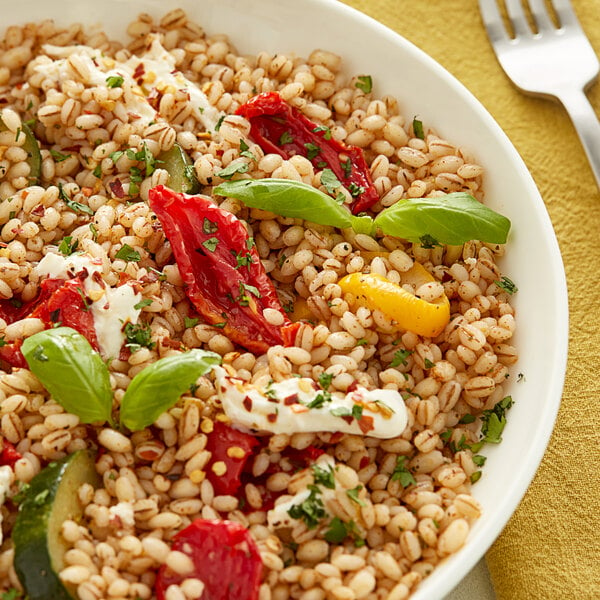 Dried whole pearl barley in a bowl of farro salad with roasted red peppers and basil.