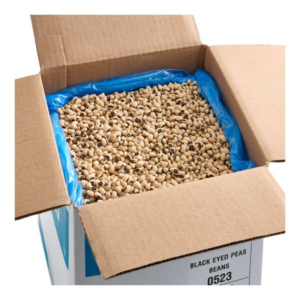 A large open cardboard box filled with dried black-eyed peas lined with a blue plastic bag.